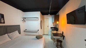 A bedroom with a bed, a desk, and a chair, a hanging light fixture, and a door leading to another room.