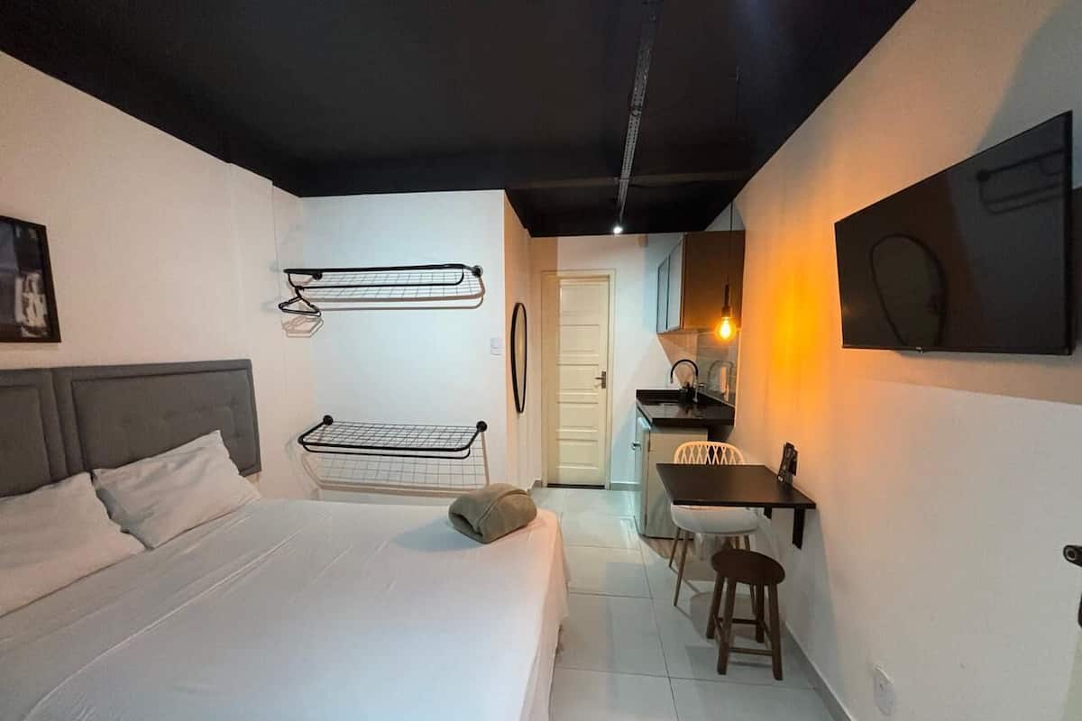 Un dormitorio con cama, escritorio y silla, una lámpara colgante y una puerta que da a otra habitación.