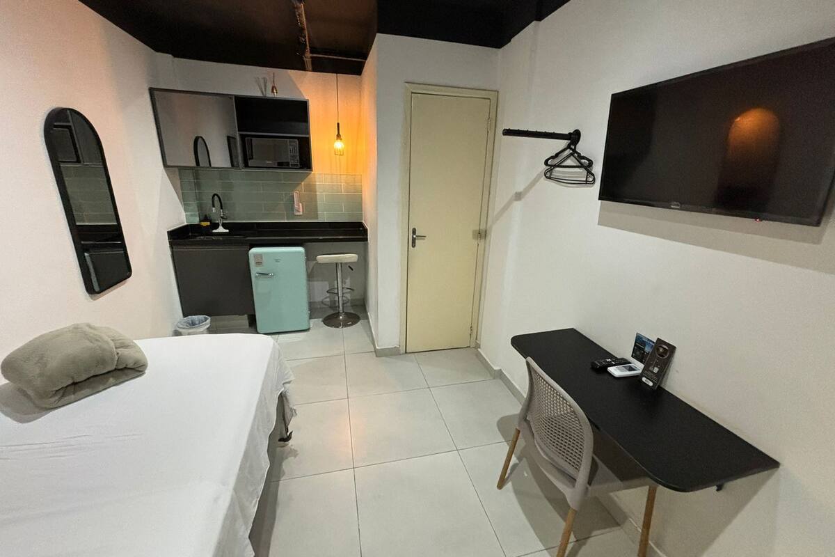 Habitación de hotel compacta con cama, kitchenette pequeña, televisor y escritorio.