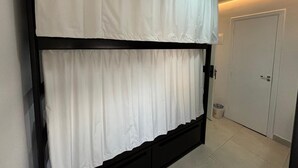 A room with a bunk bed, a door, and a trash bin.