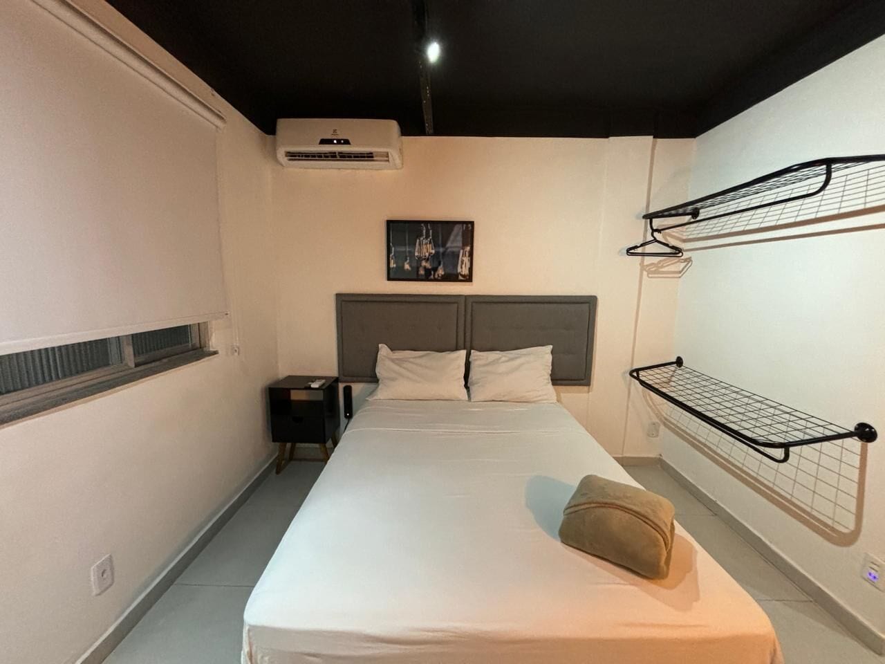 Ein Hotelzimmer mit einem Bett, einem Nachttisch, einer Wand-Klimaanlage, einem Bild an der Wand und einer Garderobe.