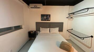 Ein Hotelzimmer mit einem Bett, einem Nachttisch, einer Wand-Klimaanlage, einem Bild an der Wand und einer Garderobe.