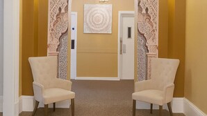 A hallway with two armchairs, a chandelier, and decorative wall panels.