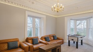 A room with leather sofas, a wooden coffee table, a foosball table, and large windows.