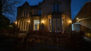 A large, historic building with multiple windows and a prominent entrance, surrounded by a well-maintained garden.
