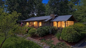 A log cabin with a stone chimney, large windows, and a porch.