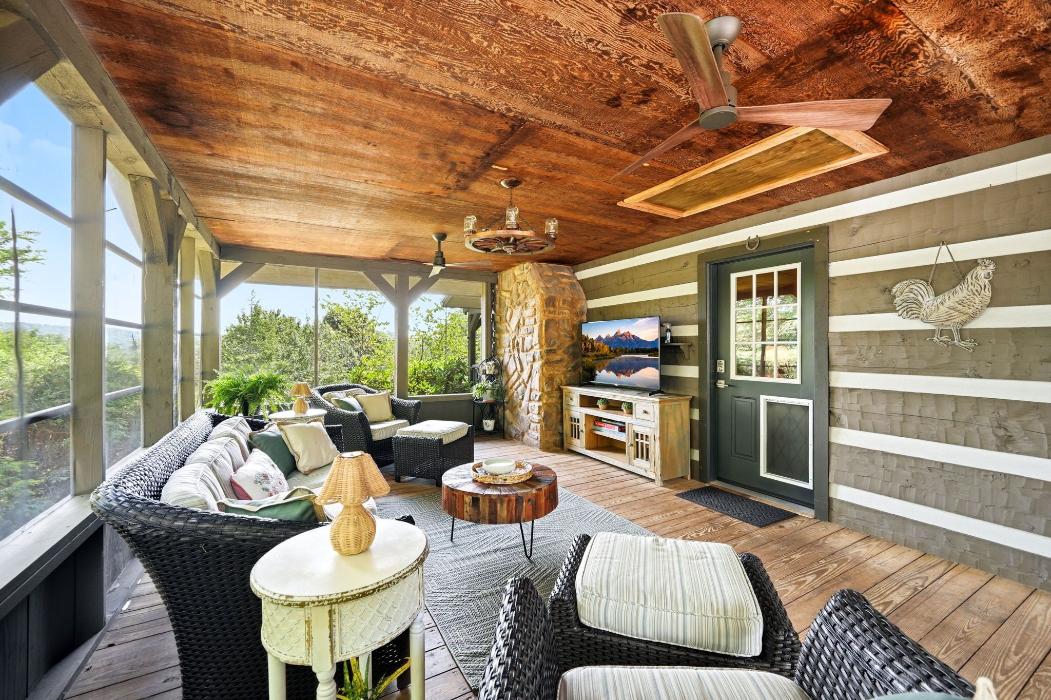 A covered outdoor seating area with wicker furniture, a stone pillar, a television, and a rooster decoration.