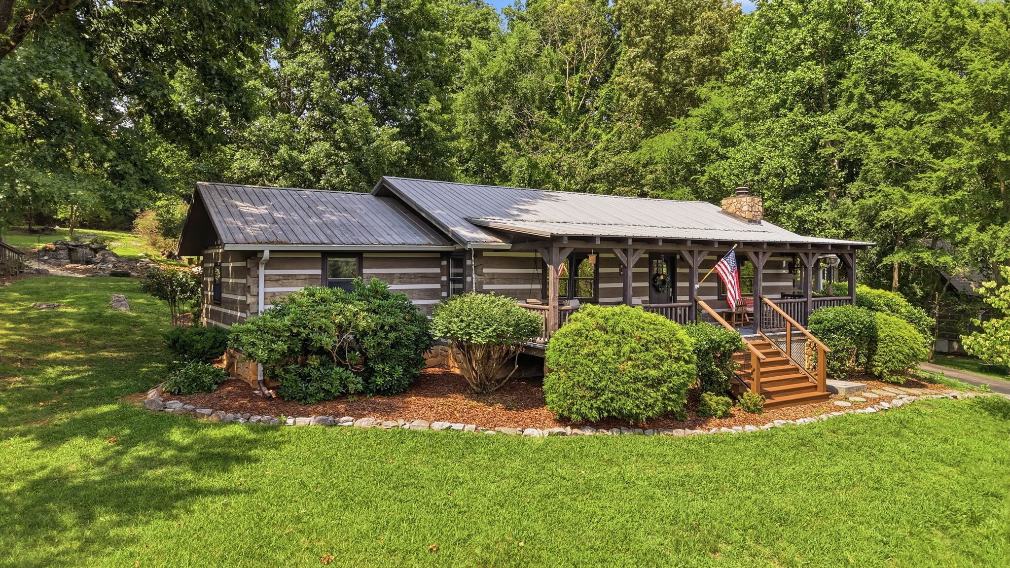 A log cabin with a porch, surrounded by well-maintained lawns and trees.