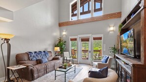 Ein Wohnzimmer mit braunem Sofa, Couchtisch, Fernseher und Kamin. Zwei Türen führen zu einem Balkon.