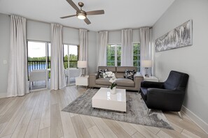 A modern living room with a sofa, coffee table, and a ceiling fan. - Resort Condo 2BR/2BA Minutes to Disney, Pool (Orlando)