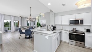 A modern kitchen with white cabinetry, a central island, and a dining area with chairs. - Resort Condo 2BR/2BA Minutes to Disney, Pool (Orlando)