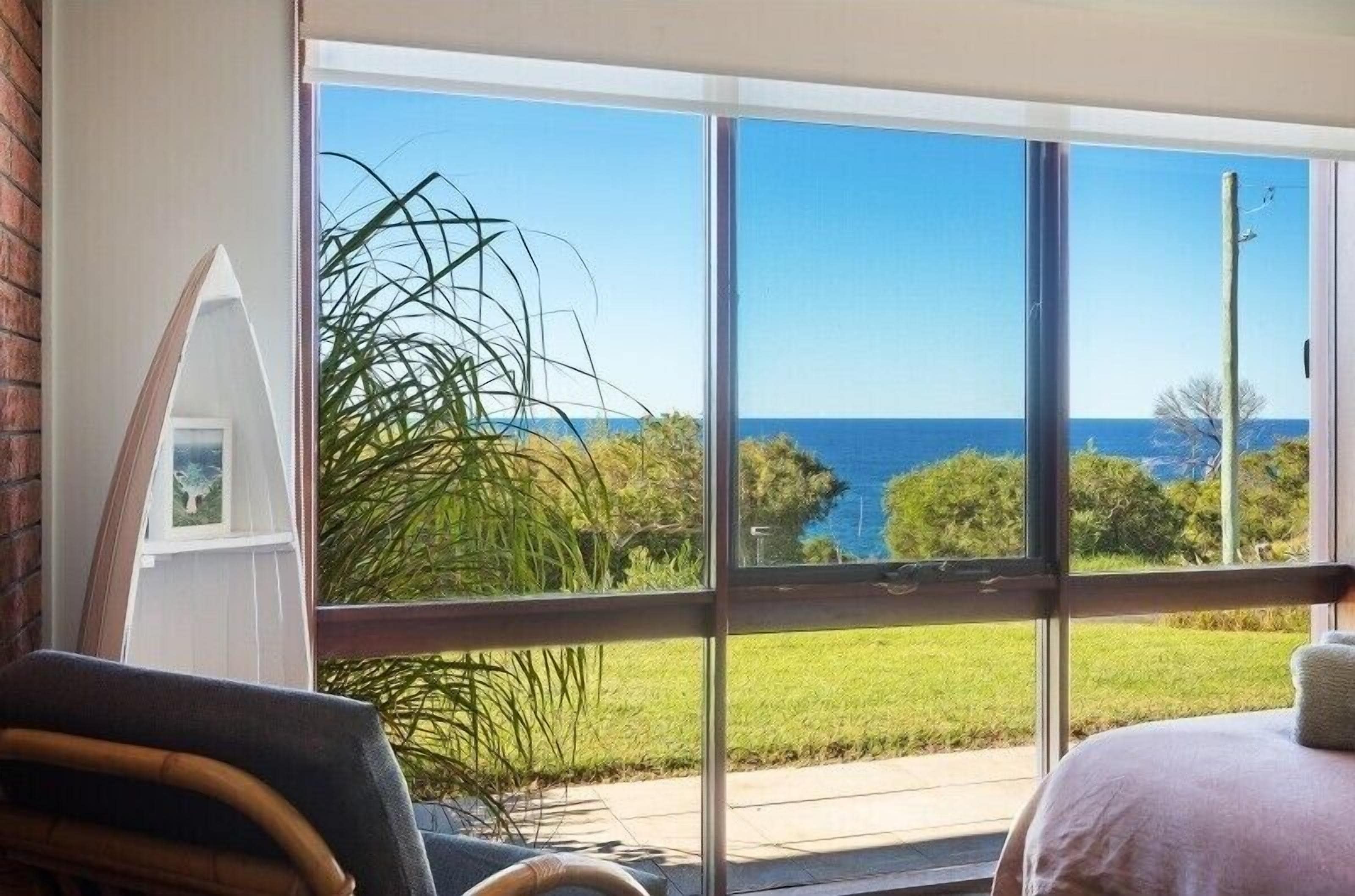 A room with a large sliding glass door leading to a balcony with a view of the ocean and greenery.