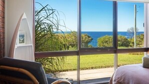 Ein Zimmer mit einer großen Schiebetür, die auf einen Balkon mit Blick auf das Meer und viel Grün führt.