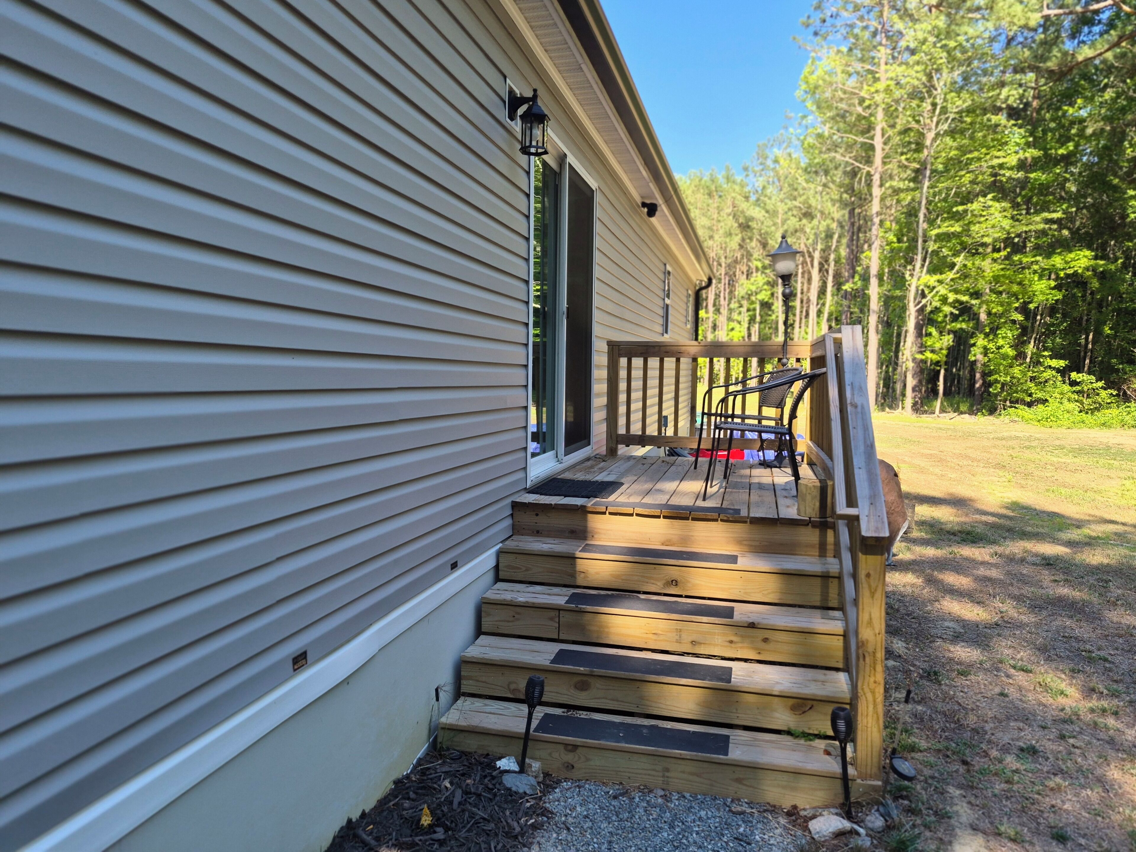 A wooden deck leading to a house with a porch and a chair.