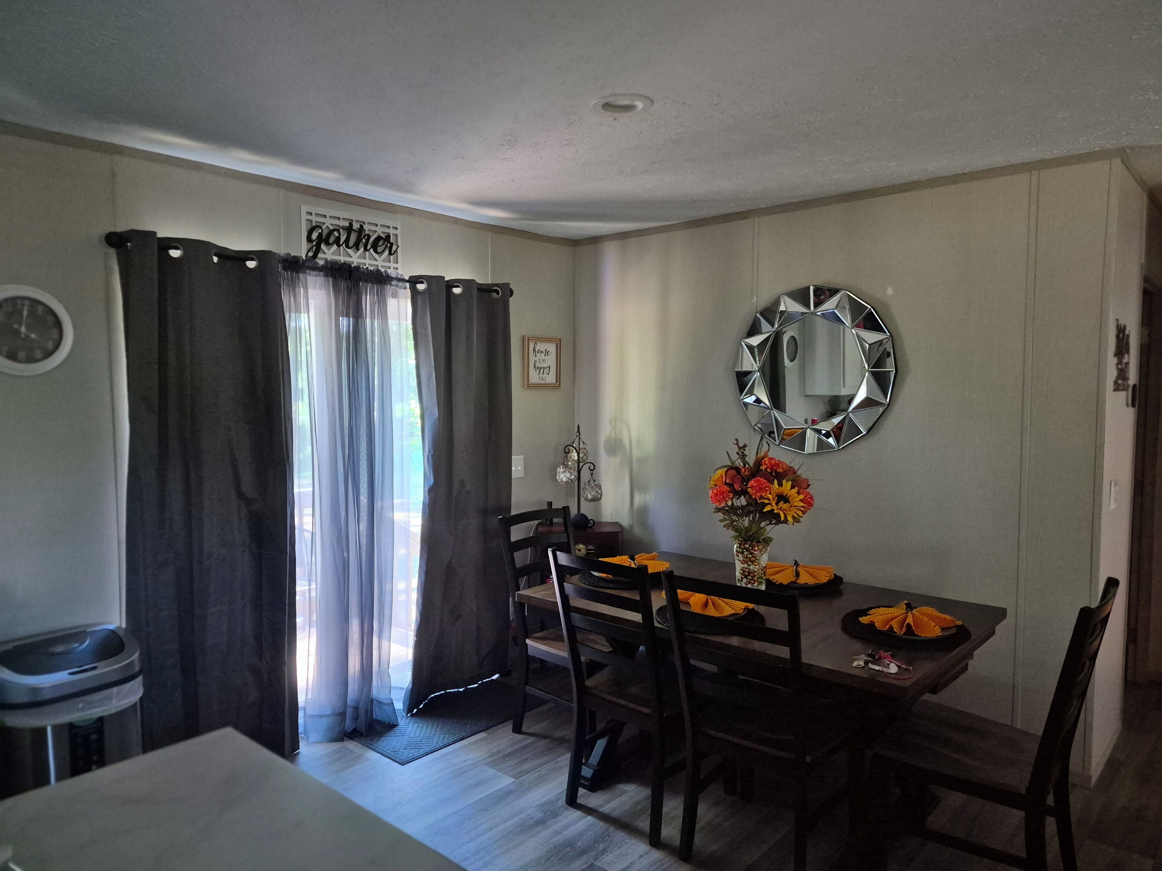 A dining area with a table, chairs, a mirror, and a sign that reads 'gather.'