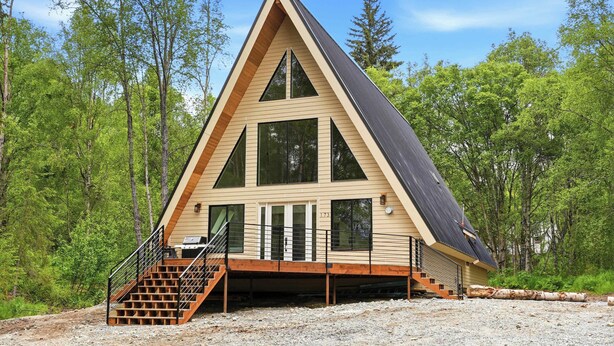 Une cabane moderne en forme de «A», dotée d’une terrasse, de grandes fenêtres et d’un escalier menant à l’entrée.