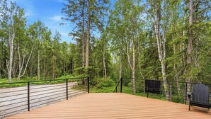 Une terrasse en bois avec des garde-corps en métal, entourée d’arbres et sous un ciel dégagé.