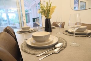 Una tavola imbandita con piatti bianchi, ciotole e bicchieri da vino, con un vaso di fiori e uno specchio appeso al muro.