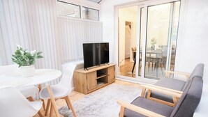 Een moderne woonkamer met een televisie, witte stoelen, een grijze bank en een houten kast.