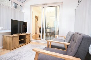 A modern living room with a flat-screen TV on a wooden stand, a grey sofa, and a glass door leading to a dining area. - Premium Family and Contractor Free Park | EV Charger (Greater Manchester)