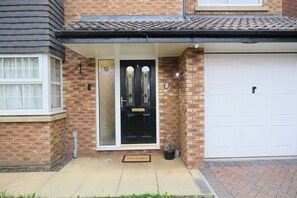 A brick house with a black front door, a garage door, and a small welcome mat. - Premium Family and Contractor Free Park | EV Charger (Greater Manchester)
