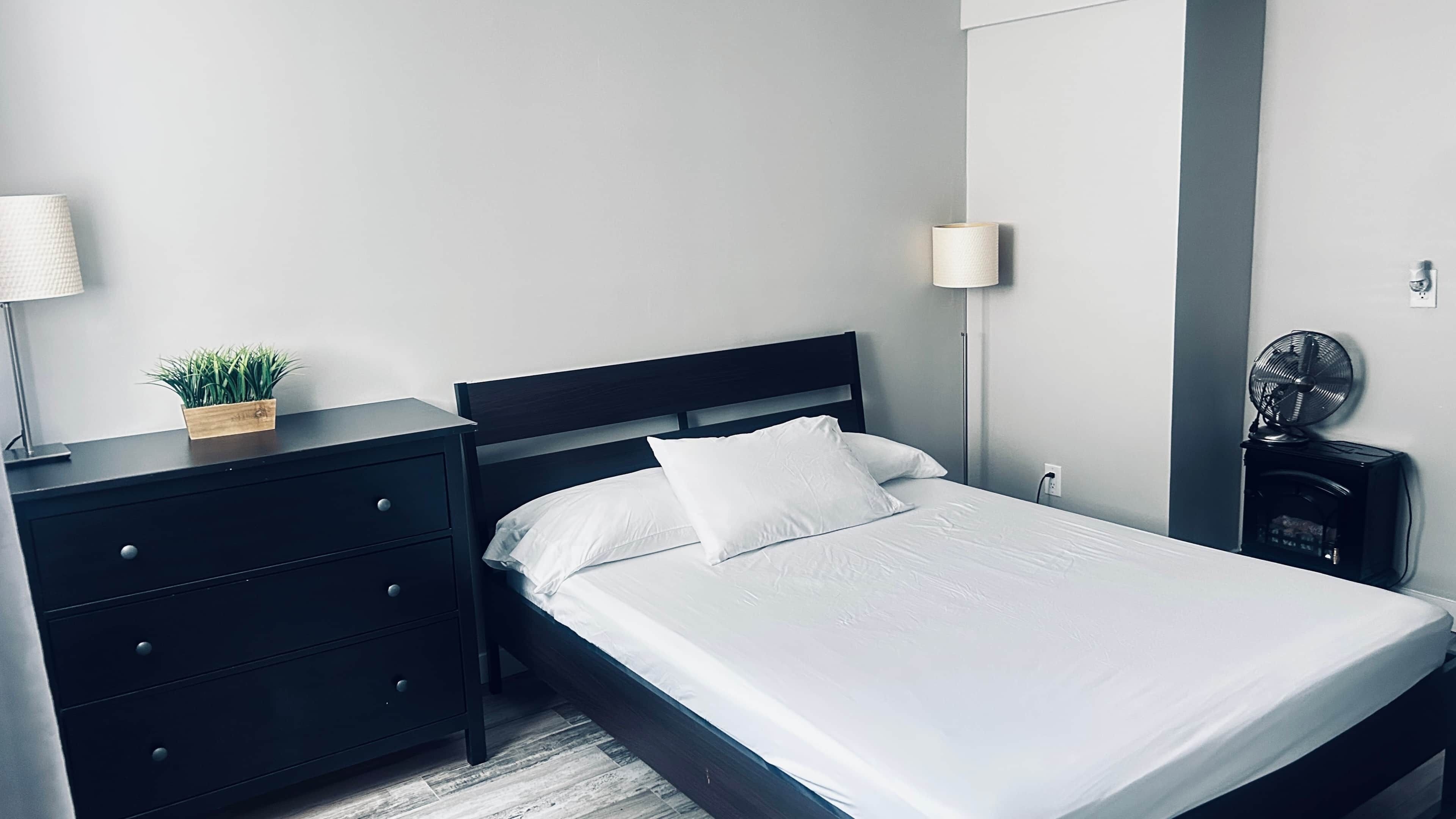 Ein modernes Schlafzimmer mit einem Bett, Nachttischen, einer Lampe, einer kleinen Pflanze und einem Ventilator.
