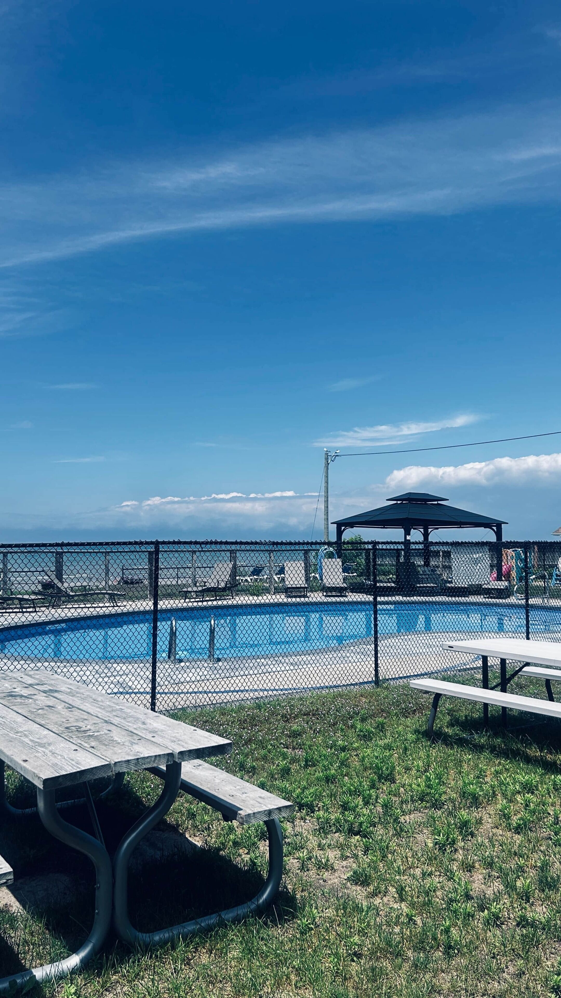 Une piscine extérieure clôturée, avec une table de pique-nique et un kiosque en arrière-plan.