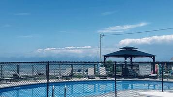 Une piscine extérieure clôturée, avec une table de pique-nique et un kiosque en arrière-plan.