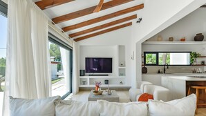 Una sala de estar moderna con un televisor de pantalla plana grande, sofás blancos, una mesa de centro y una zona de cocina con ventana.