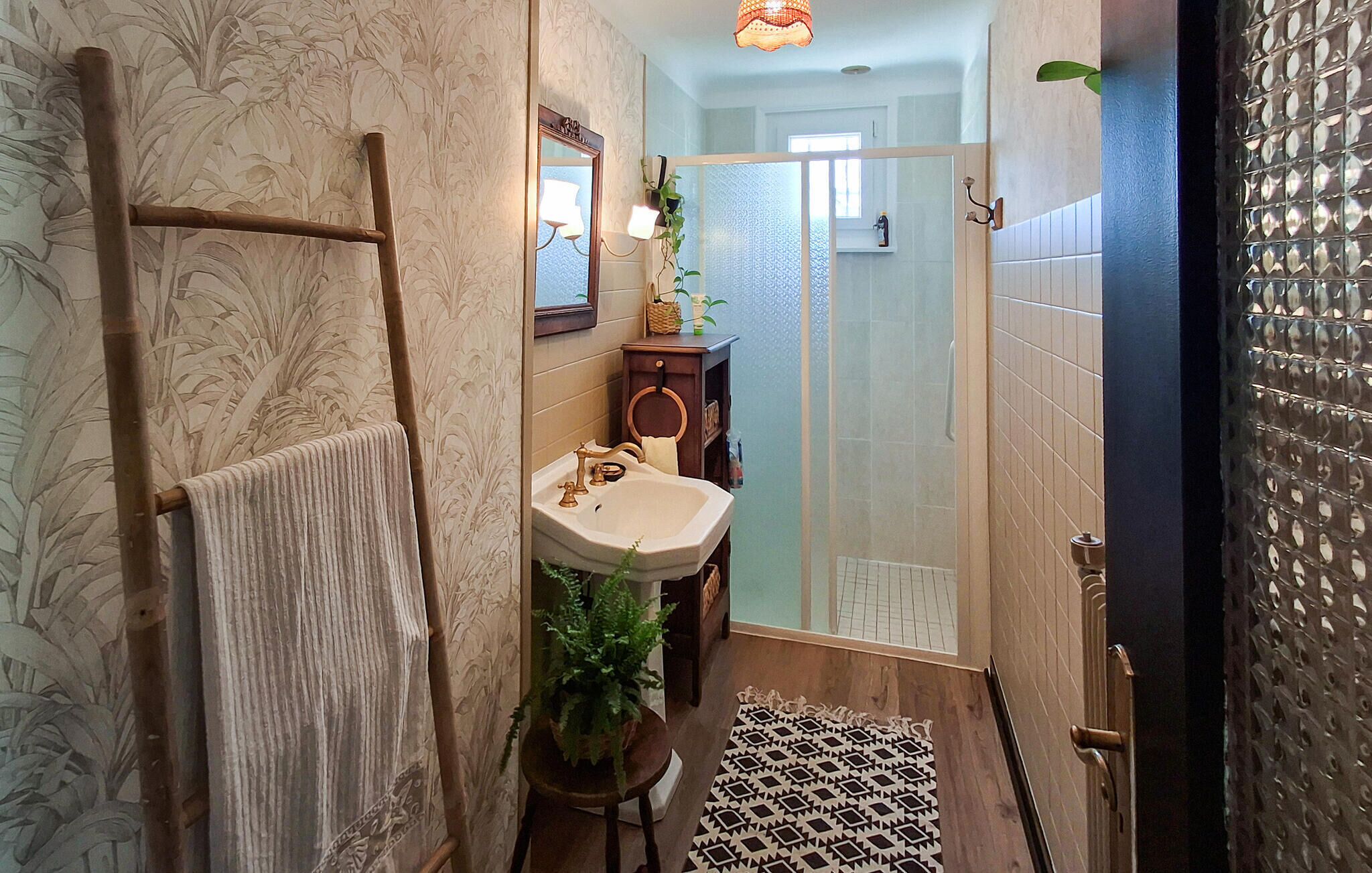 Un baño con una escalera de madera, un lavamanos, un espejo, una planta en maceta y una alfombra estampada.