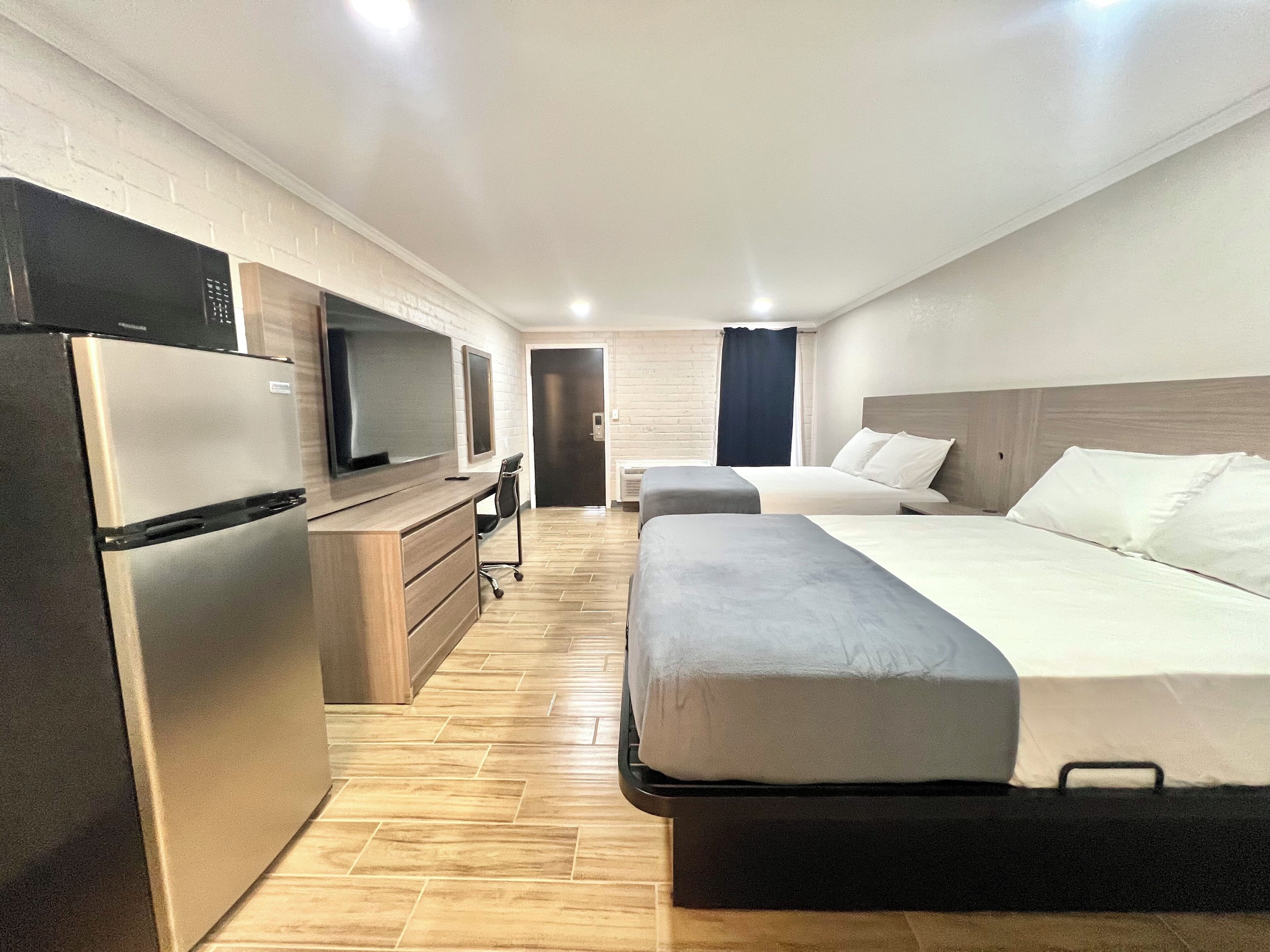 Ein modernes Hotelzimmer mit Küchenzeile, einem Bett, einem Schreibtisch und einem Fernseher.