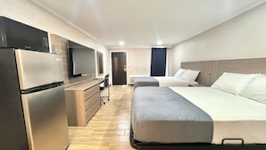 A modern hotel room with a kitchenette, a bed, a desk, and a television.