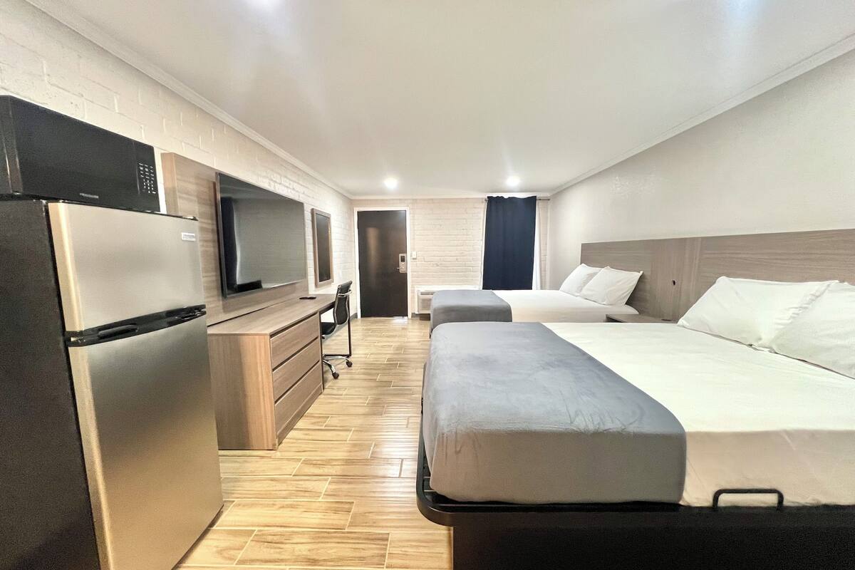 Quarto de hotel moderno com cozinha compacta, uma cama, escrivaninha e televisão.