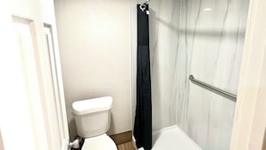 A bathroom with a toilet, a shower with a glass door, and a white bathtub.