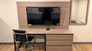A modern office space with a large flat-screen TV, a desk with drawers, a black office chair, and a mirror on the wall.