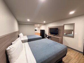 Ein Hotelzimmer mit zwei Betten, einem Schreibtisch, einem Fernseher und einer kleinen Küchenzeile im Hintergrund.