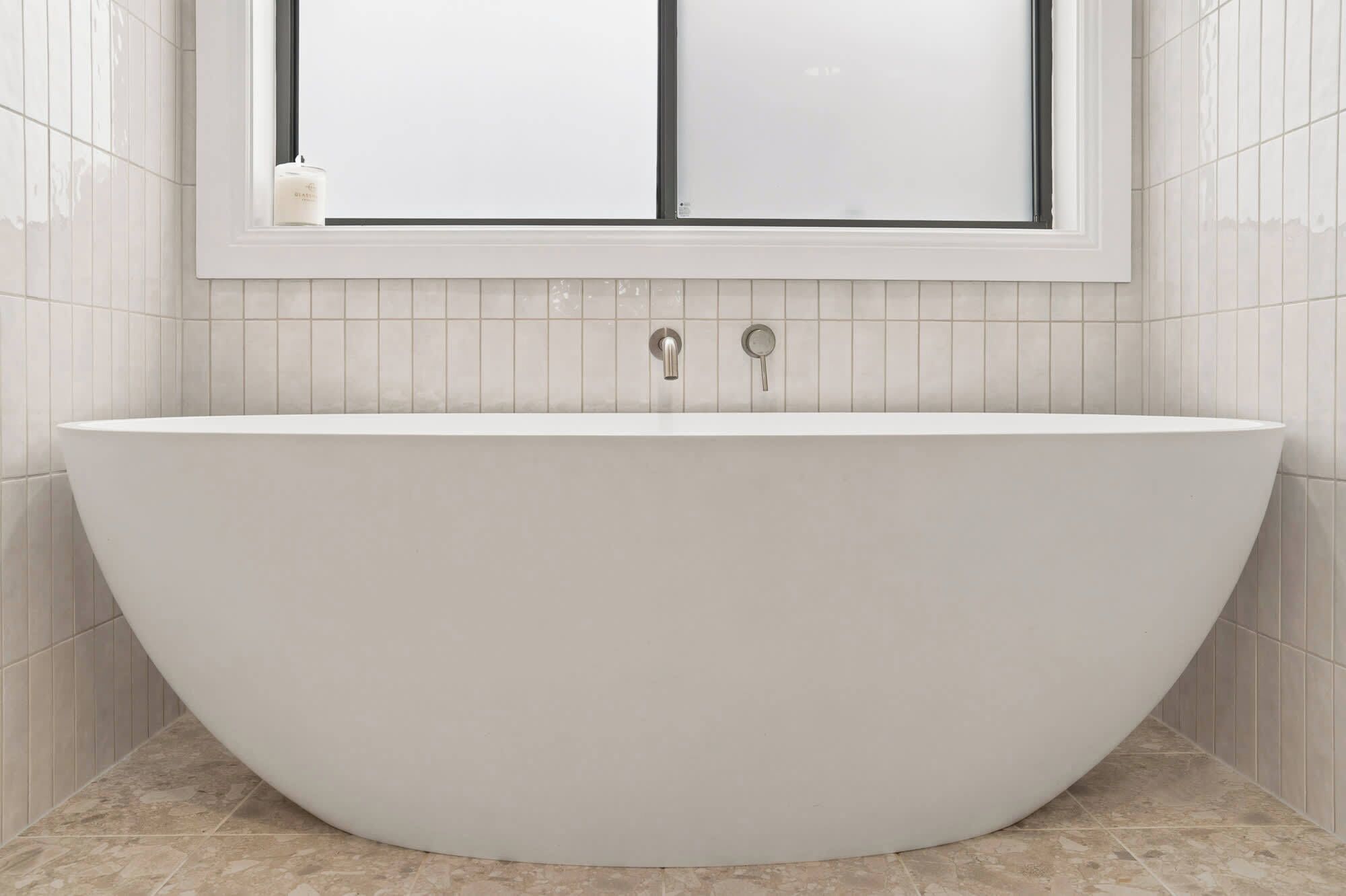 Une salle de bain moderne avec une baignoire sur pieds, une fenêtre située au-dessus et des murs recouverts de carreaux.