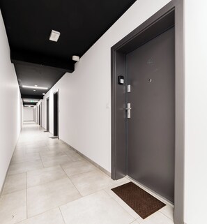 A hallway with a series of doors, a brown doormat, and a ceiling light fixture. - Nadolnik Cozy Studio (Poznań)