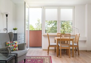 Huoneessa on ruutukuviollinen sohva, ruokapöytä tuoleineen, pieni ruukussa oleva kasvi ja näkymä liukuoven läpi.