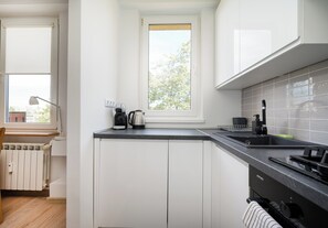 Moderni keittiö, jossa on valkoiset kaapit, musta työtaso, ikkuna, josta avautuu näkymä puita kohti, ja sisäänrakennettu liesi.
