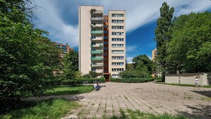 Een meerlaags woongebouw met balkons, een geplaveid binnenterrein en omliggend groen.