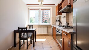 Een keuken met een eettafel, stoelen, een koelkast en een raam met uitzicht op gebouwen.