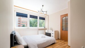 Een slaapkamer met een bed, een bureau, een radiator, een raam met zonwering, een deur en een plafondlamp.