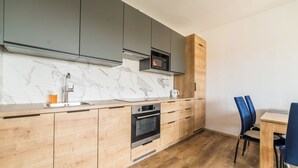 Une cuisine moderne avec des meubles gris, un pare-feu en marbre, un four à micro-ondes encastré et une table à manger en bois avec des chaises bleues.