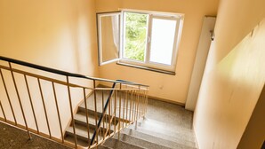 Un escalier avec une rampe en métal, une fenêtre donnant sur la verdure et un mur sobre.