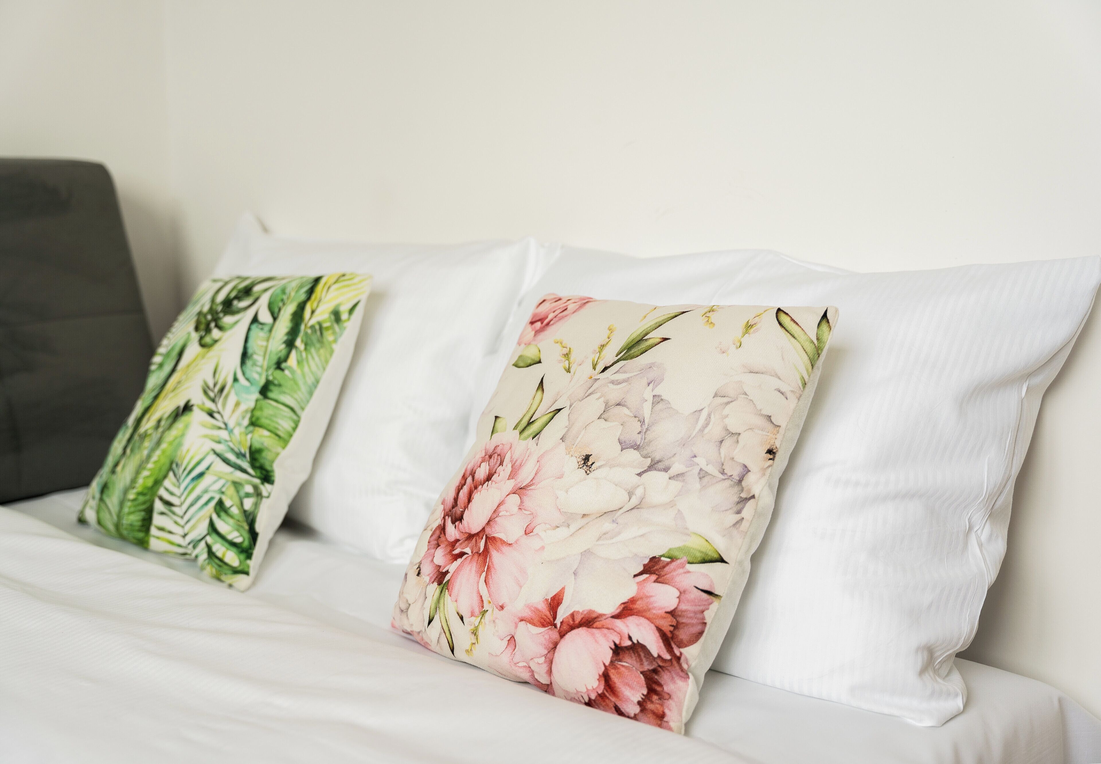 A bed with white bedding and two decorative pillows with floral patterns.