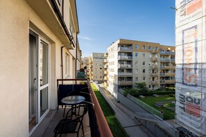 Un balcón con mesa y sillas, vista a un edificio residencial y un área verde con una cerca.