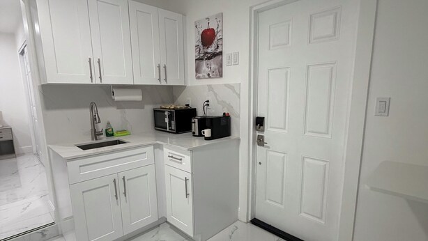 A compact kitchen with white cabinets, a microwave, a toaster, and a sink.