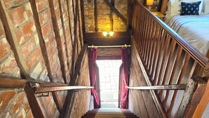Uma escada de madeira com uma parede de tijolos de um lado e uma cama com cabeceira do outro.