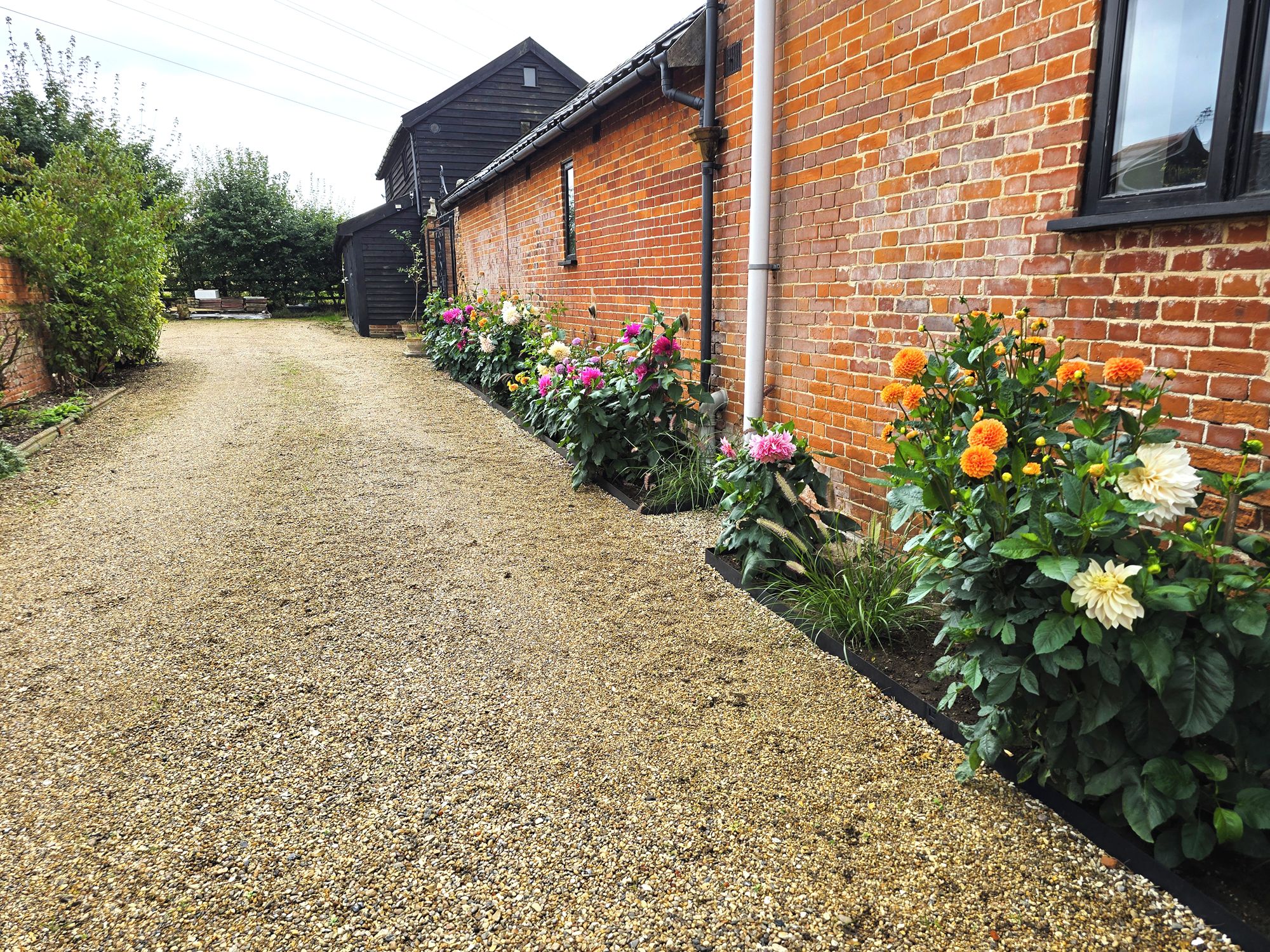 A gravel driveway leading to a brick house with flower beds on either side.